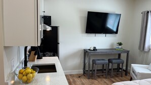 A compact hotel room with a kitchenette, a dining area with a table and two chairs, a bed, and a TV mounted on the wall. - Winney Hill Studios #5 of 8 Studios - Full Renovation, 1 mile to ASV (Oneonta)