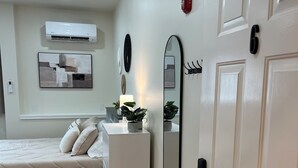 A bedroom with a bed, bedside table, mirror, and a door with a number.