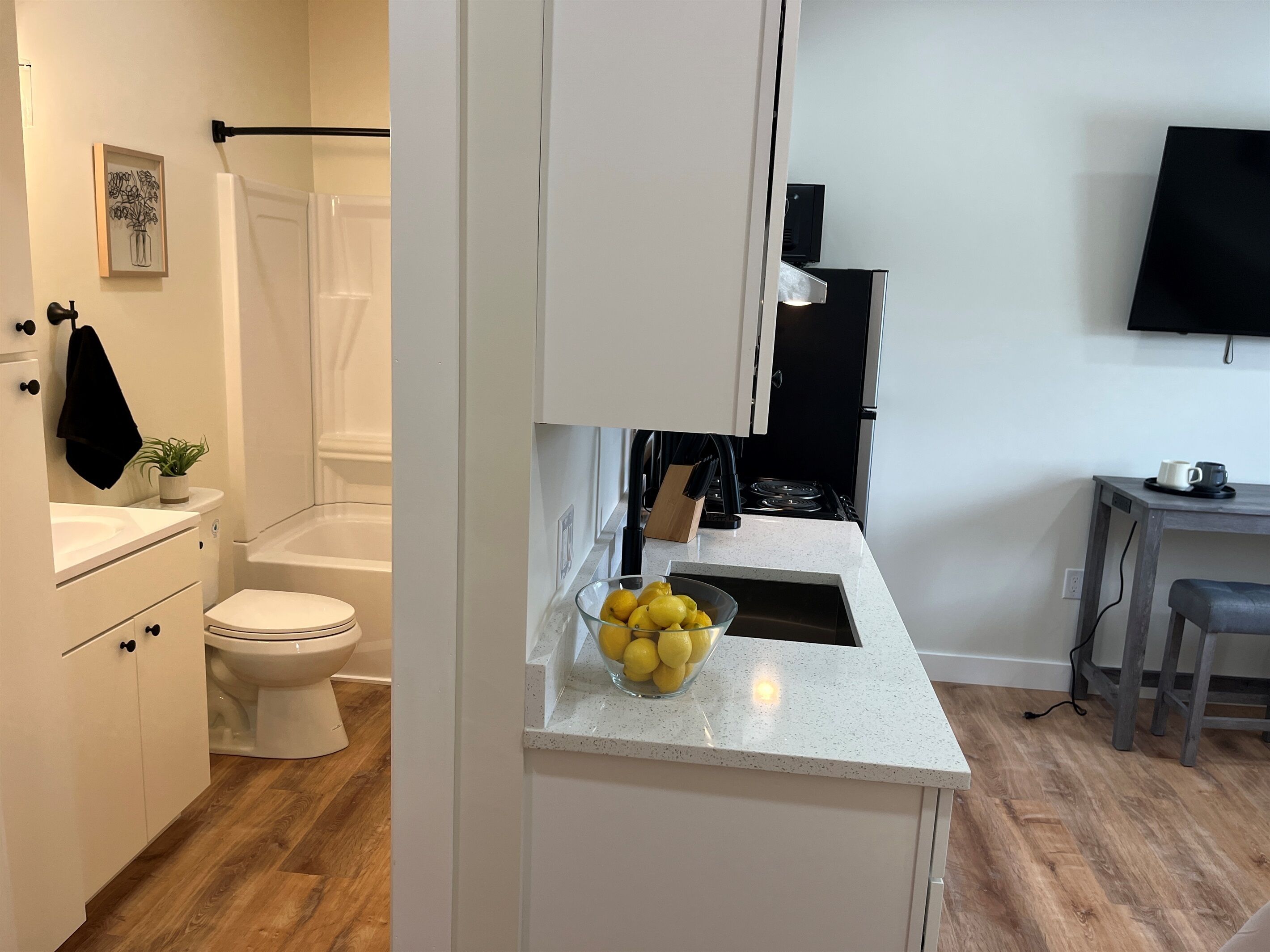 A modern kitchen with white cabinets, a countertop with a bowl of lemons, a stove, and a small table with a cup.