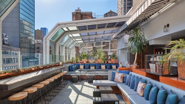 A rooftop bar with a glass enclosure, seating areas, and bar stools.