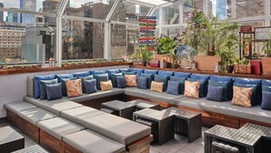 A modern rooftop lounge with a glass ceiling, city views, and a variety of seating options.