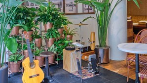 A room with a guitar, potted plants, a drum set, and a table with chairs.