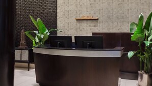 A reception desk with a dark wood finish, a reception sign above it, and potted plants on either side.