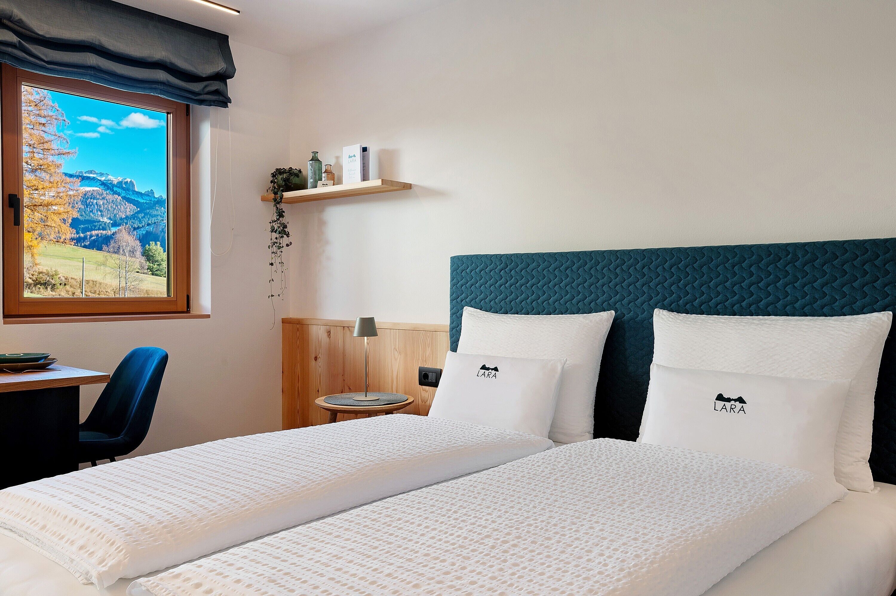 Une chambre d’hôtel équipée d’un lit, d’un bureau, d’une chaise, d’une lampe et d’une fenêtre donnant sur un paysage montagneux.