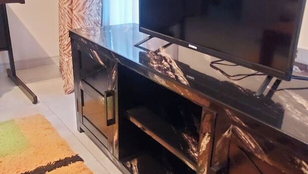 A modern living room with a large flat-screen TV on a black marble console, a patterned rug, and a wooden cabinet.