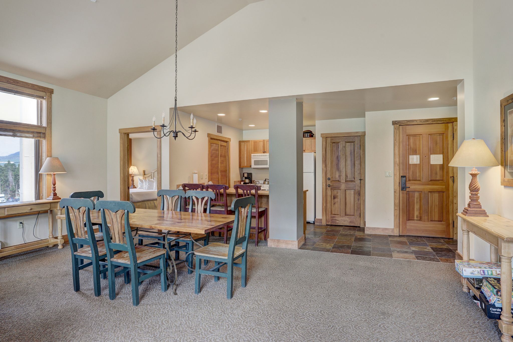 A spacious dining area with a wooden table and chairs, a chandelier, and a view of the kitchen in the background.