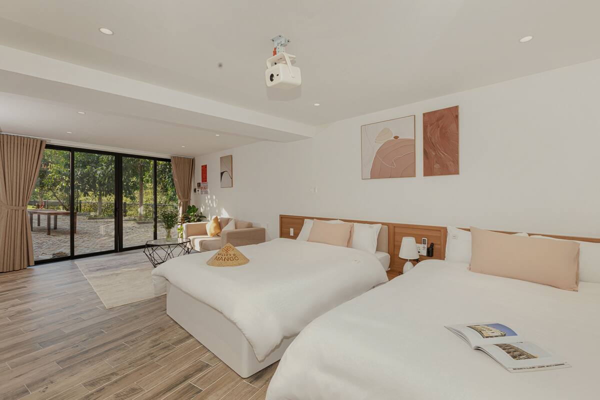 Une chambre d’hôtel moderne avec deux lits, une grande fenêtre et un projecteur.
