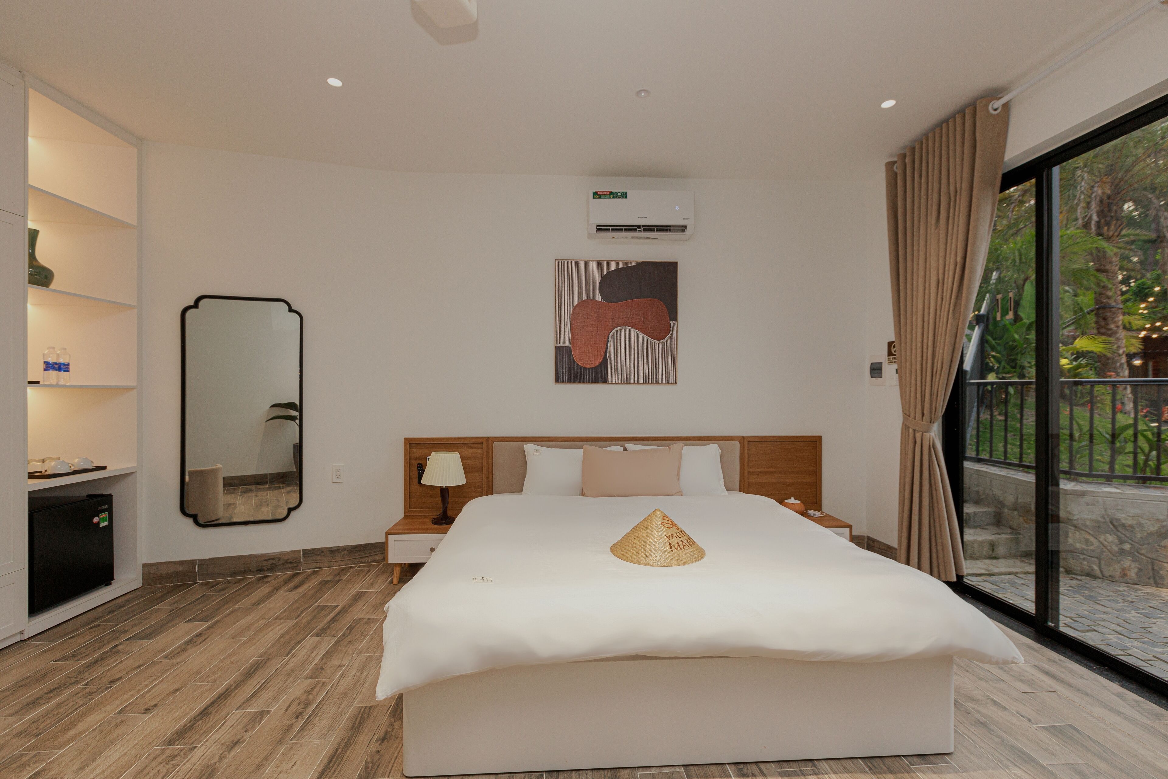 Une chambre d’hôtel moderne avec un grand lit, une table de chevet avec une lampe, un climatiseur fixé au mur et une grande fenêtre avec des rideaux.