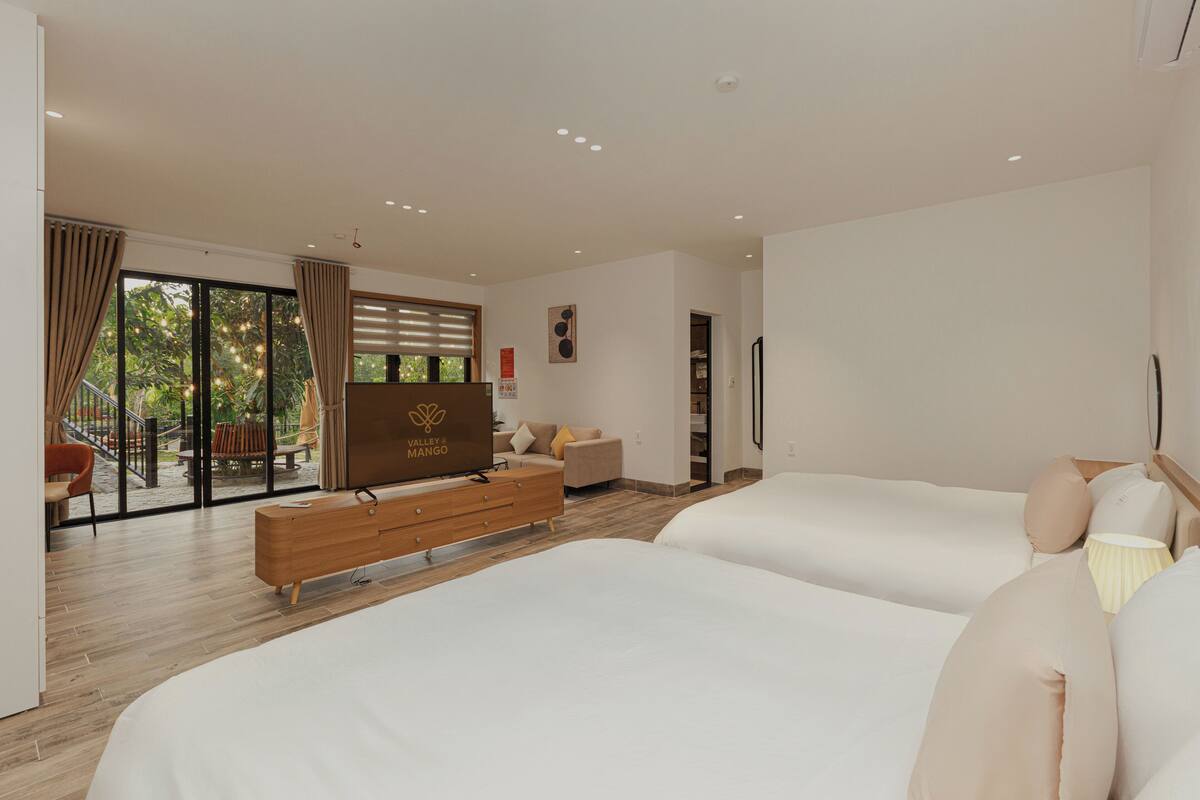 Une chambre d’hôtel avec deux lits, une commode en bois, une télévision et un balcon avec des meubles d’extérieur.