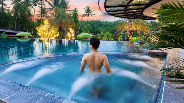 A man in a hot tub with a view of palm trees and a sunset. - VALLEY DE MANGO VILLA (Hue)