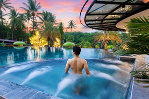 Un homme dans un jacuzzi, avec vue sur des palmiers et un coucher de soleil.