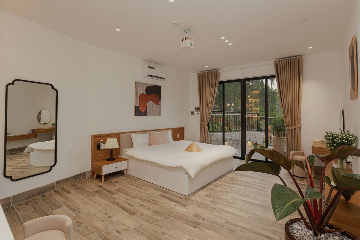 Une chambre d’hôtel moderne avec un grand lit, une table de chevet, un miroir et une plante en pot.