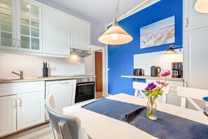 A modern kitchen with white cabinets, a built-in oven, and a blue accent wall. - Apartment '1' with Modern Country-Style Kitchen (Cuxhaven)