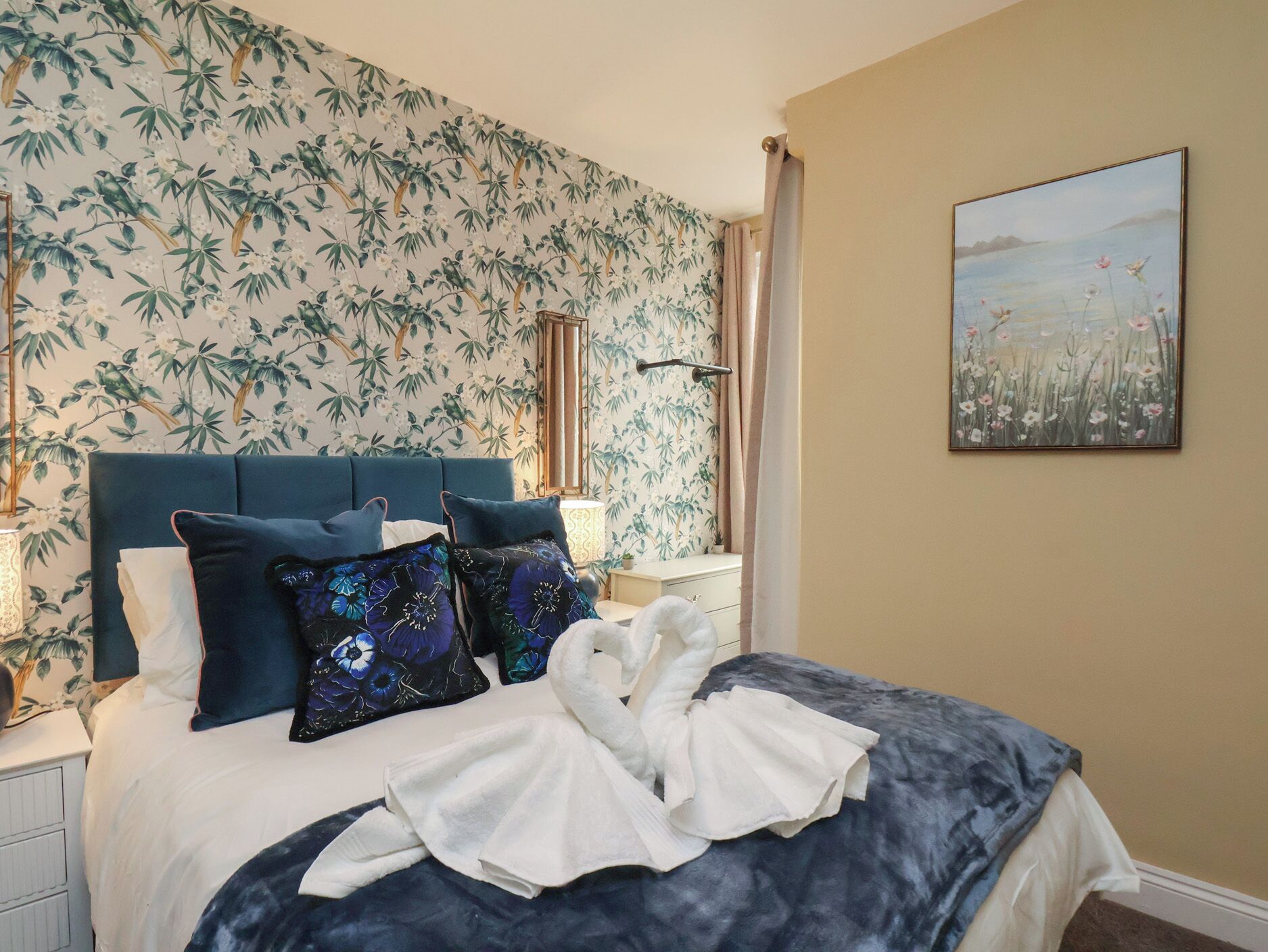 A bedroom with a bed, pillows, a nightstand, a lamp, and a painting on the wall.