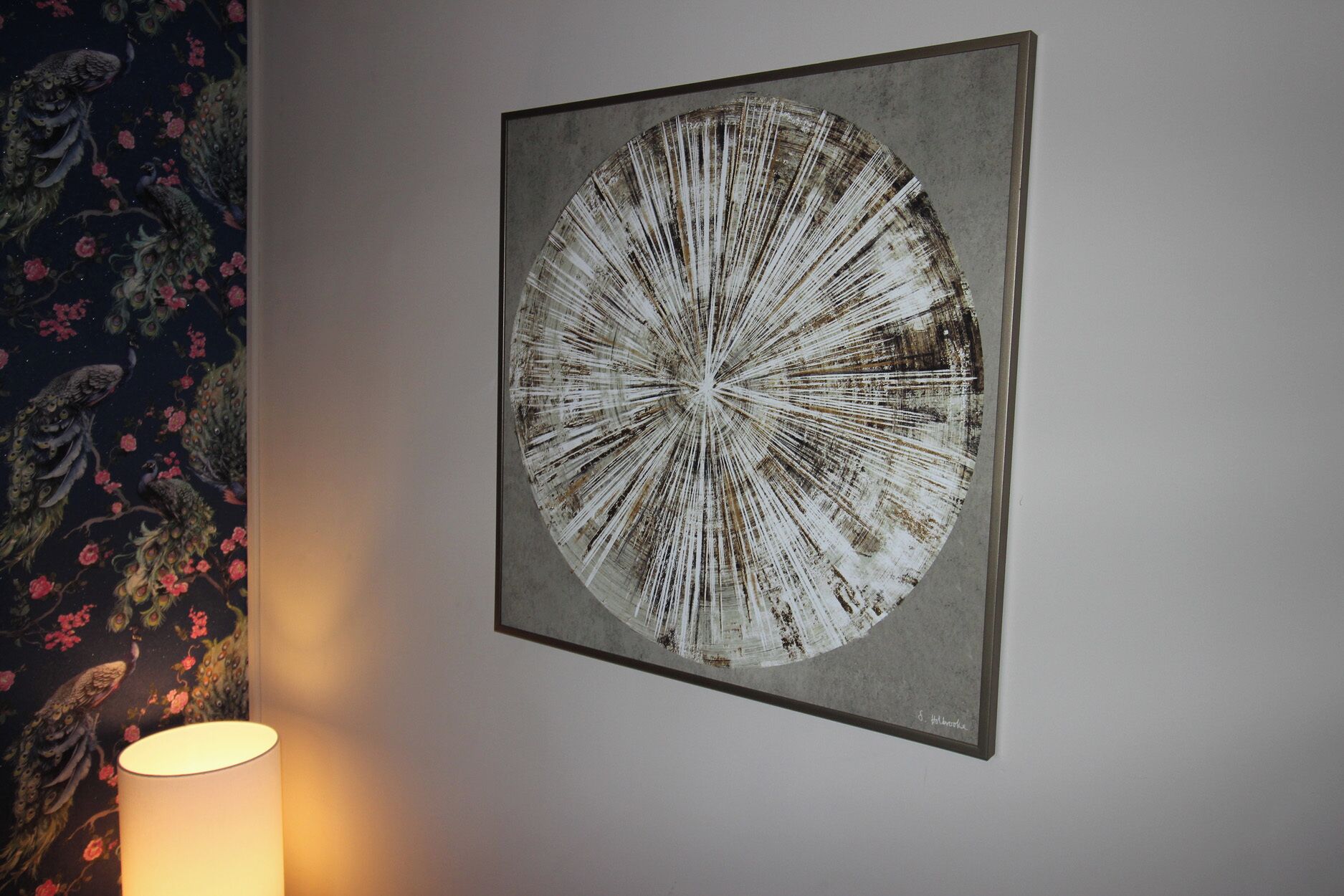 A framed artwork on a wall, a lamp, and a floral wallpaper pattern.