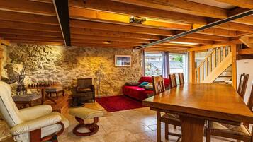 A cozy room with a stone wall, a wooden dining table, and a red sofa.