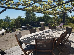 Un espace de restauration en plein air avec une table ronde en bois et des chaises, entouré d’une pergola couverte de plantes grimpantes.
