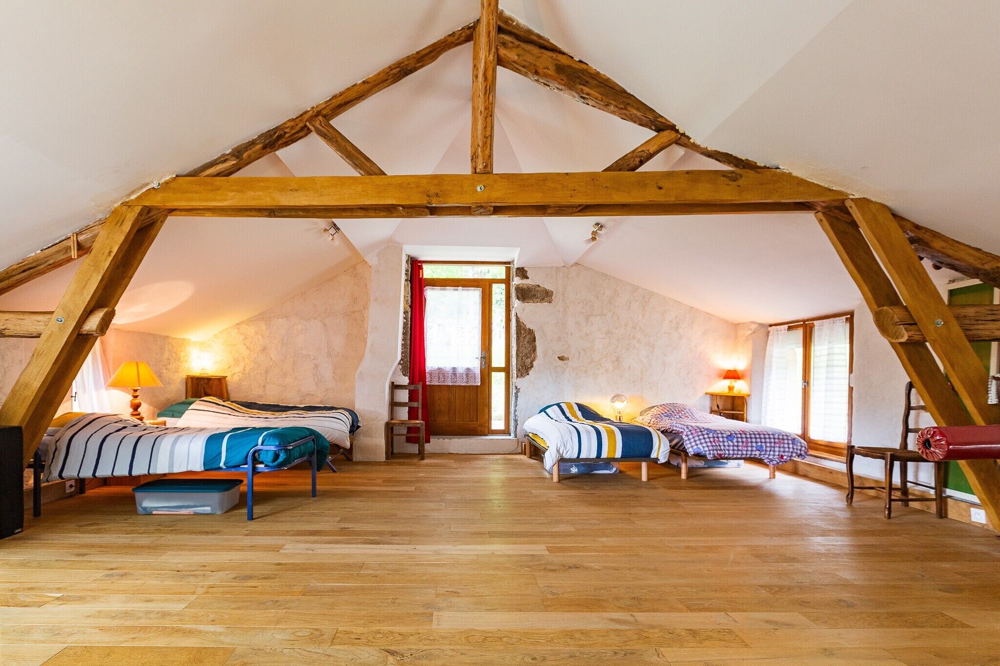 Une chambre mansardée avec des poutres en bois, deux lits, une échelle et une fenêtre.
