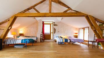 Une chambre mansardée avec des poutres en bois, deux lits, une échelle et une fenêtre.
