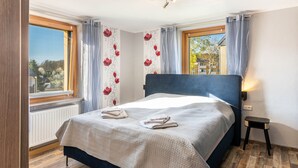 Un dormitorio con cama, ventana, radiador y un taburete pequeño.