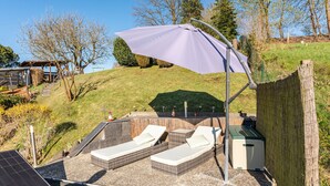 Un espacio al aire libre y luminoso para relajarse, con sillones de mimbre, un paraguas grande y un calentador pequeño.