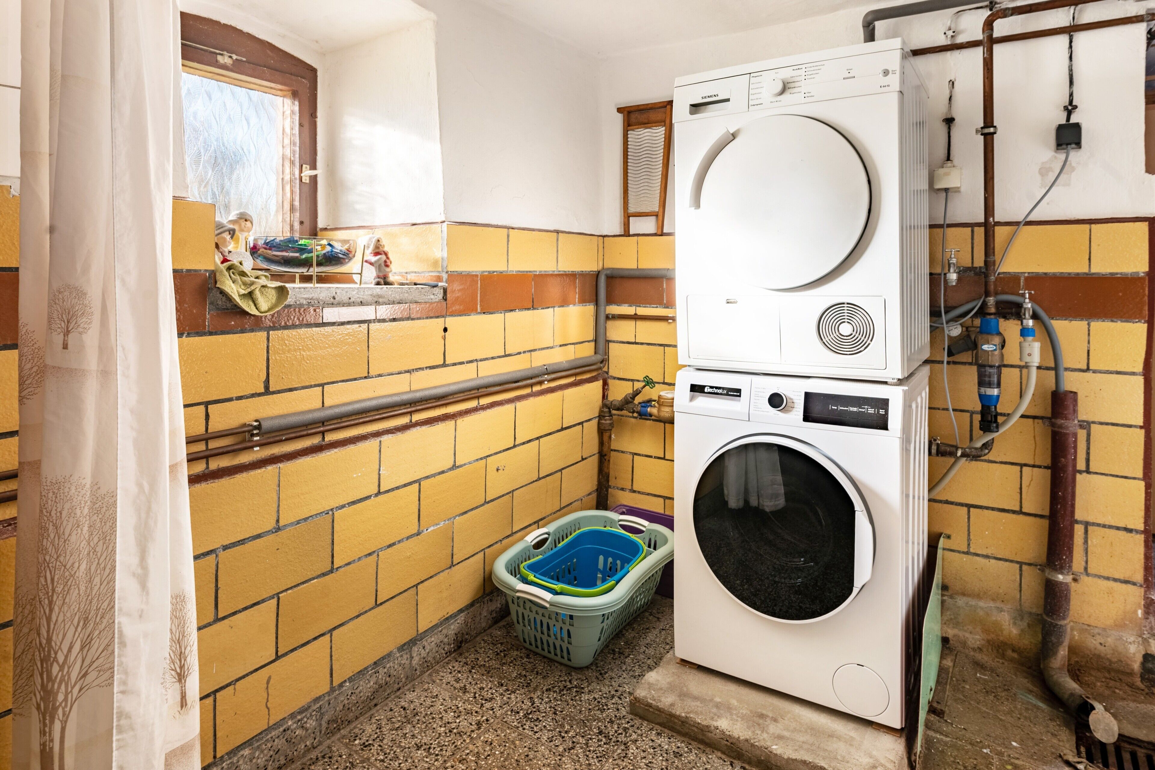 A laundry room with a washing machine and dryer, a window with a view, and a tiled wall.