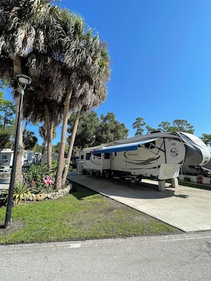 A large RV parked in a well-maintained area with palm trees and a clear blue sky. - Blue Lagoon. Enchanting RV in sunny Naples (Naples)