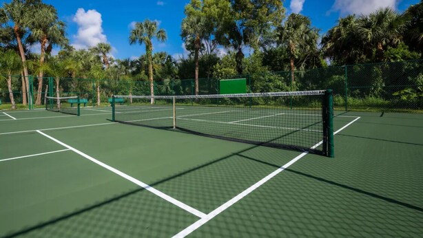 Un campo da tennis con una rete, circondato da alberi e un cielo sereno.