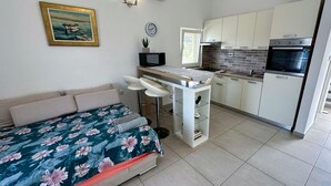 Een compacte kamer met een bed, een klein keukenhoekje en een eethoek.