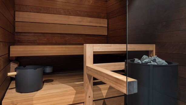 Sauna, jossa on puiset lauteet, musta roskakori ja kivillä täytetty astia.