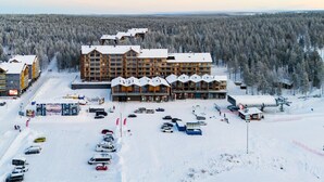 Monikerroksinen hotelli, jonka takana kohoaa hiihtohissi, ja hotellia ympäröi lumipeitteinen metsä.