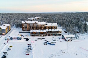 Ein mehrstöckiges Hotel mit Sessellift im Hintergrund, umgeben von einem verschneiten Wald.