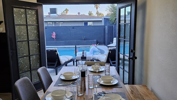 Un coin repas avec vue sur une piscine située dans le jardin, un lustre moderne et une cloison en verre décorée d’autocollants représentant des papillons.