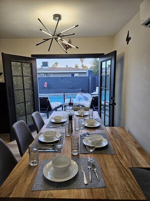 Un coin repas avec vue sur une piscine située dans le jardin, un lustre moderne et une cloison en verre décorée d’autocollants représentant des papillons.