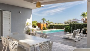 Ett utomhusområde med en pool, ett bord och stolar, en pergola och utsikt över en bostadsbyggnad.