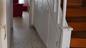 Een hal met betegelde vloer, een trap met houten treden, en een rode stoel op de achtergrond.
