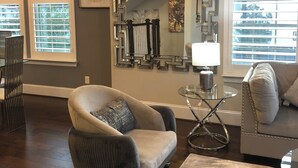 A living room with a large mirror, a sofa, a chair, and a coffee table. - Modern Upscale 3-bedroom house in Houston energy corridor (Houston)