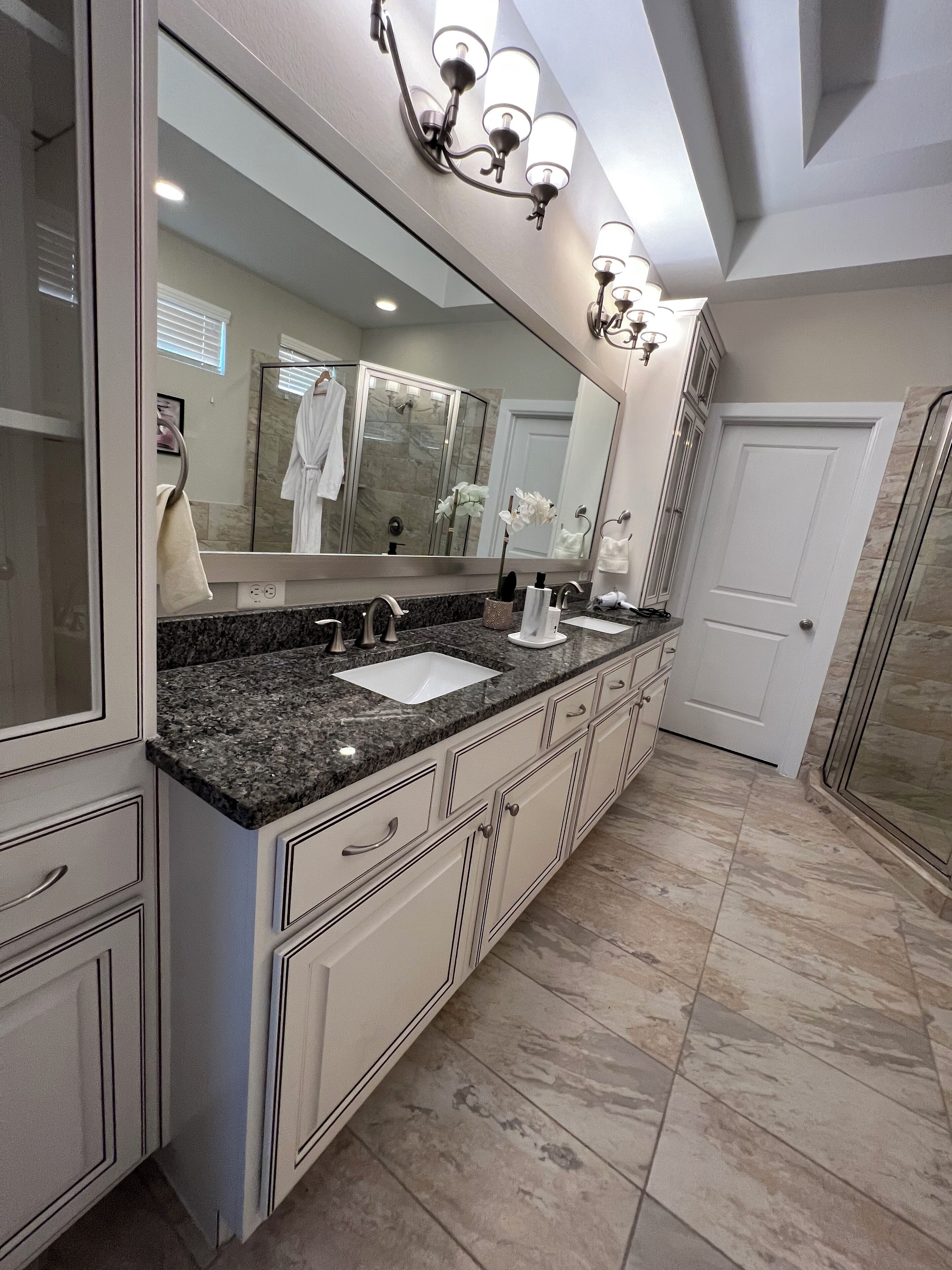 A spacious bathroom with a double sink vanity, a large mirror, and a walk-in shower.
