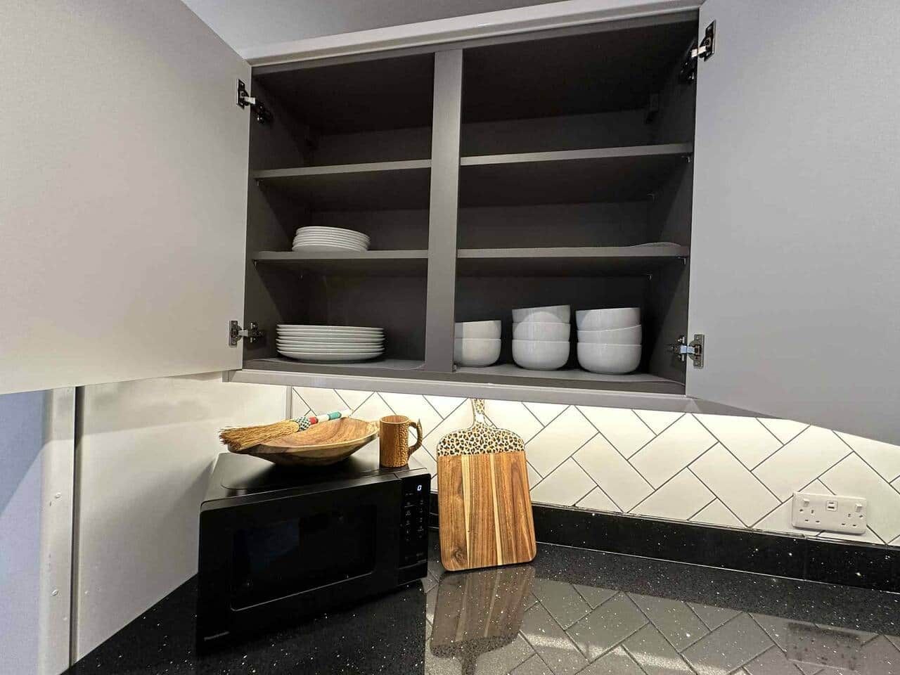 A kitchen with a microwave, a cutting board, and a basket on the counter.