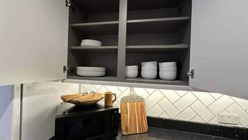 A kitchen with a microwave, a cutting board, and a basket on the counter.