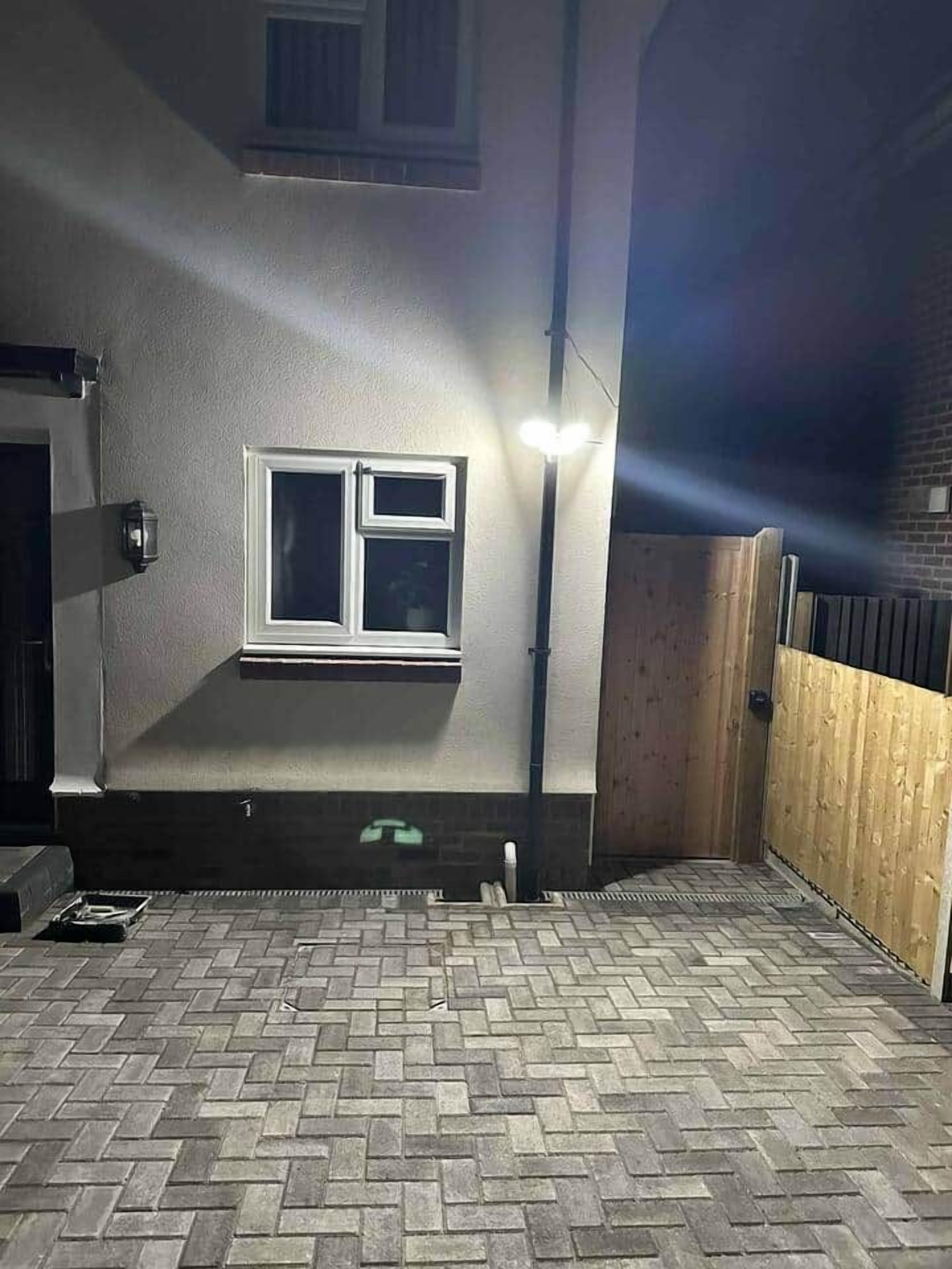 Uma área externa coberta com uma janela, piso de tijolos e cerca de madeira.