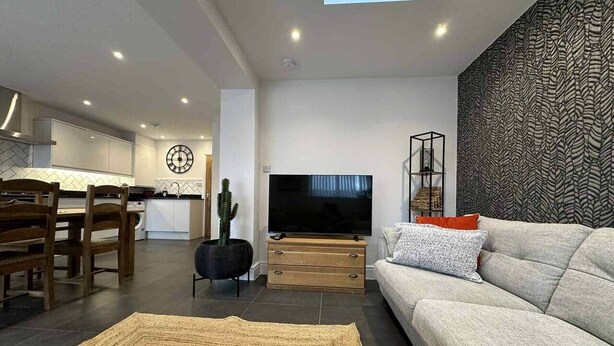 Un salon moderne avec un téléviseur à écran plat, un canapé, un coin repas avec des chaises et une cuisine en arrière-plan.