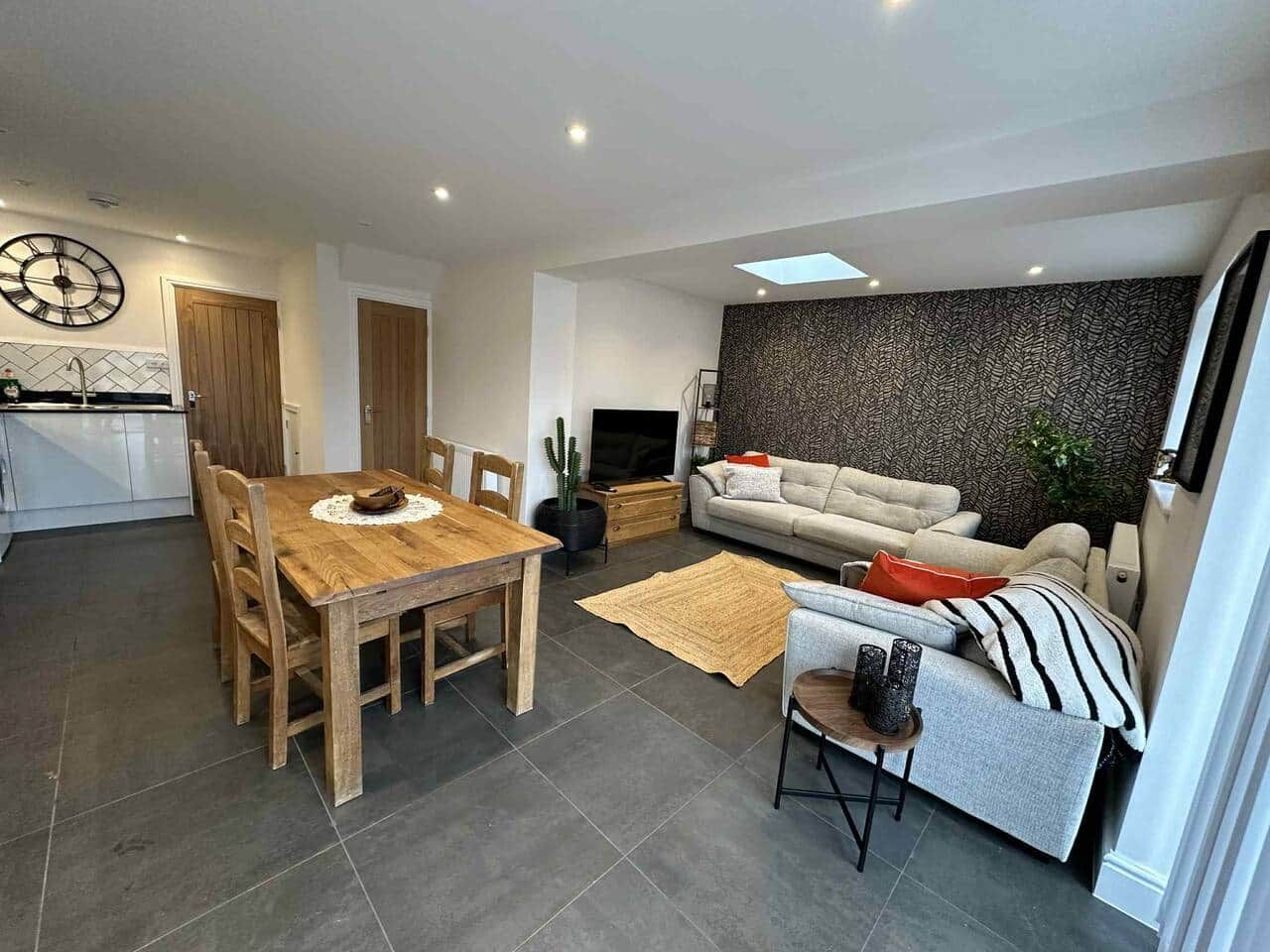 A modern living room with a wooden dining table, a sofa, and a patterned wall.