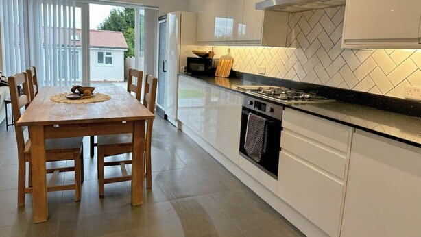 A modern kitchen with white cabinets, a wooden dining table, and a large window. - Contractor &Leisure stay.4BR all en-suite +Parking (Portsmouth)