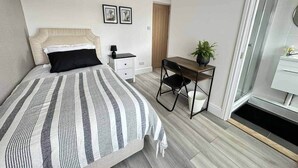 Une chambre à coucher avec un lit, un bureau, une chaise, une table de chevet et une plante en pot.