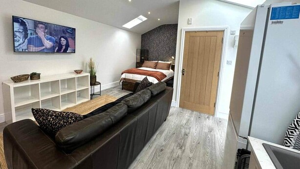 Un salon moderne avec un canapé, un téléviseur fixé au mur et un lit à l’arrière-plan.