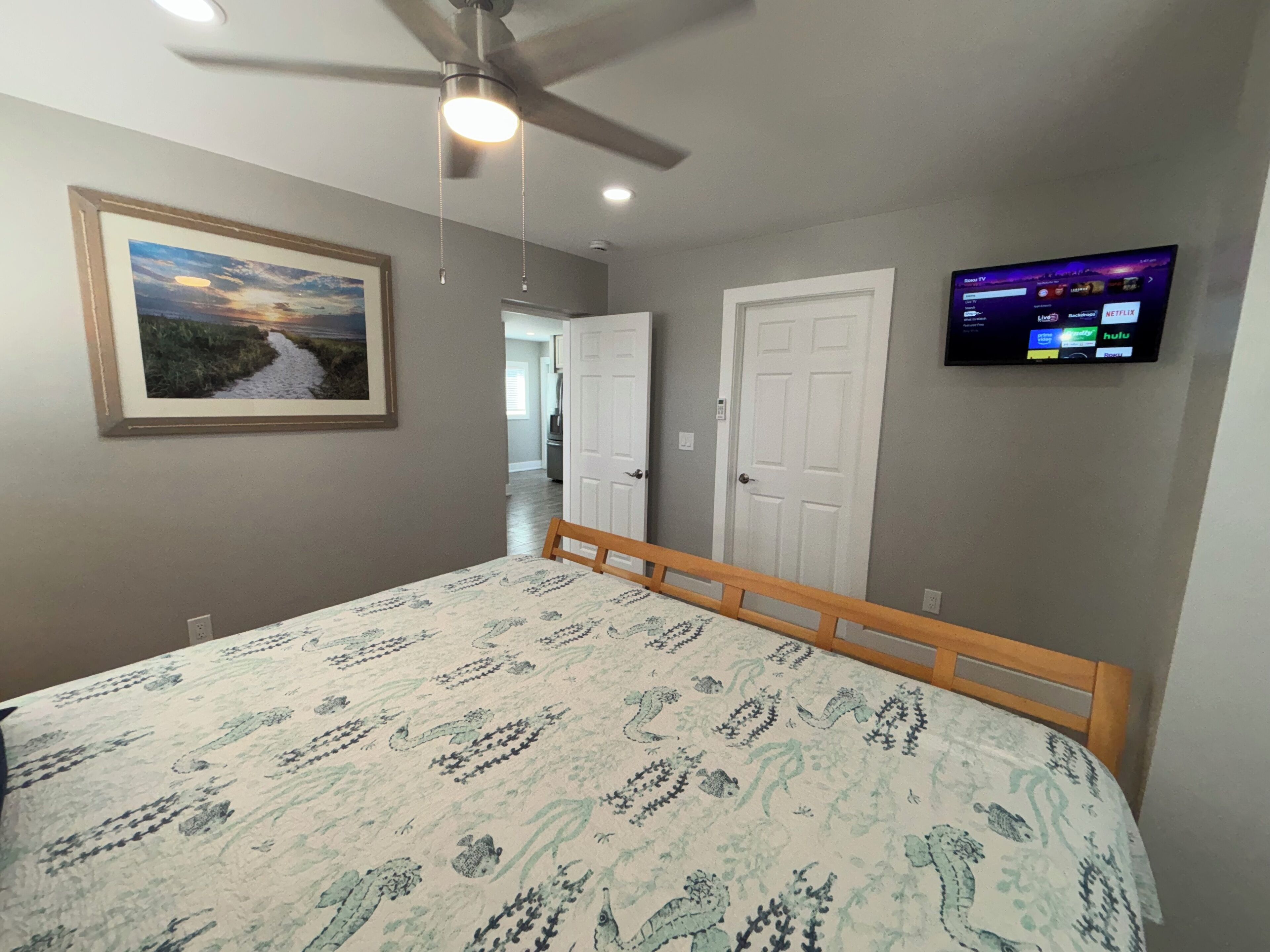A bedroom with a bed, a ceiling fan, a TV mounted on the wall, and a framed picture on the wall.