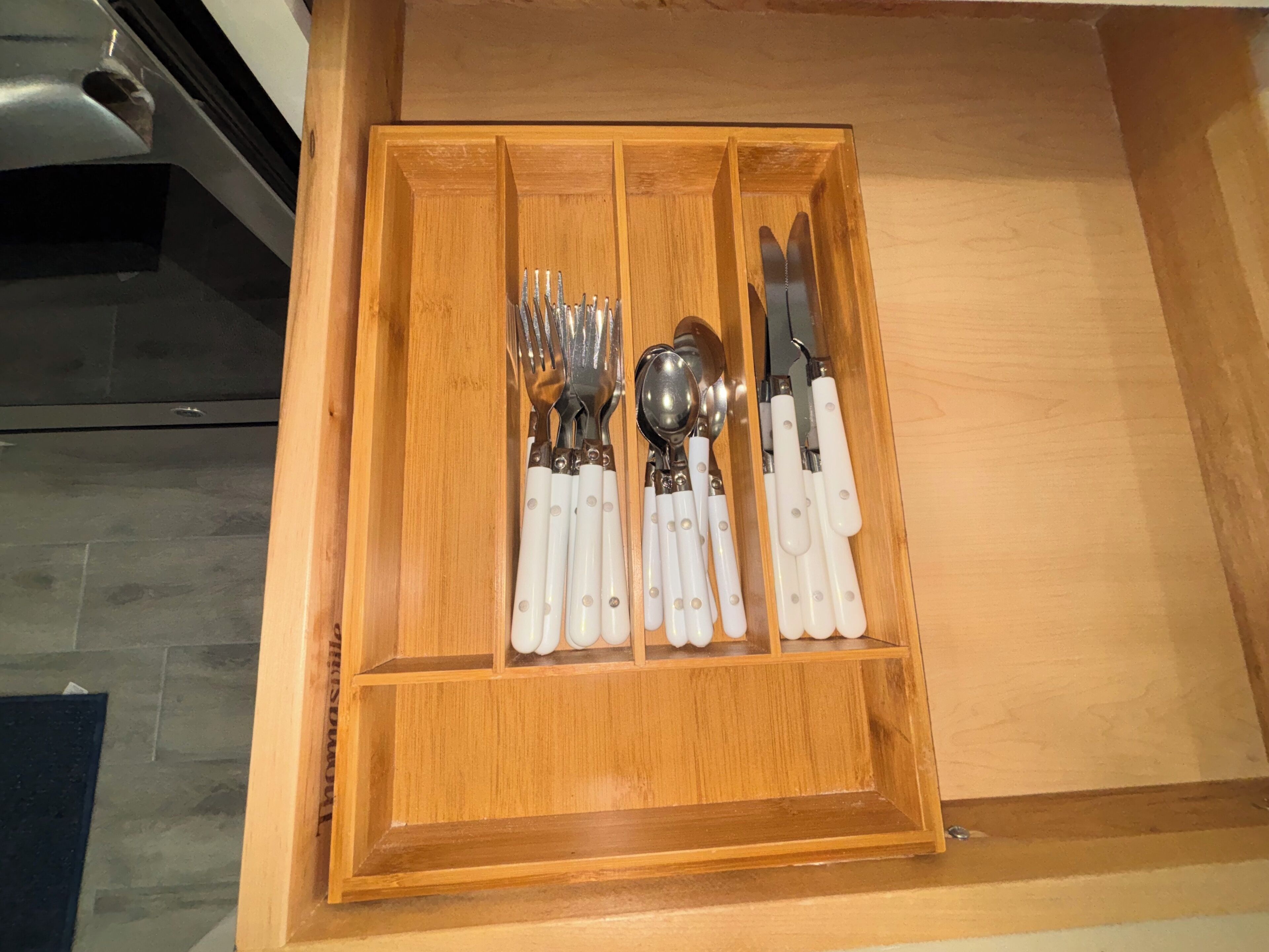 Un tiroir en bois, doté de compartiments, contenant divers ustensiles de table.
