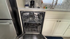 An open dishwasher in a kitchen with white cabinets and a marble backsplash. - New -1st Floor Spacious Kit W&D Close 2 Everything 3Mi To Beach Sleeps 4 KingBed (Bonita Springs)