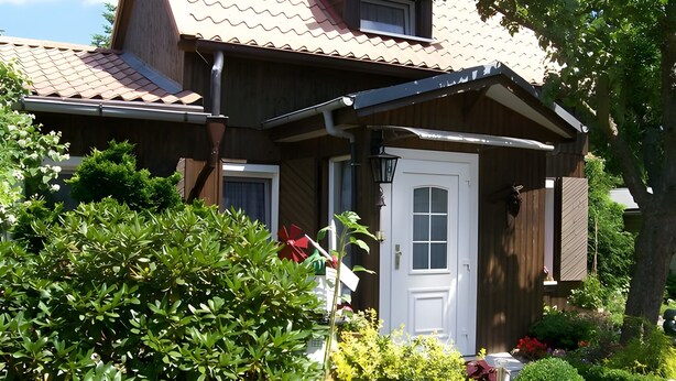 A wooden house with a white door, a small porch, and a garden with various plants and flowers. - Holiday Home 'Blumenhof' with Shared Garden, Balcony and Wi-Fi (Wandlitz)